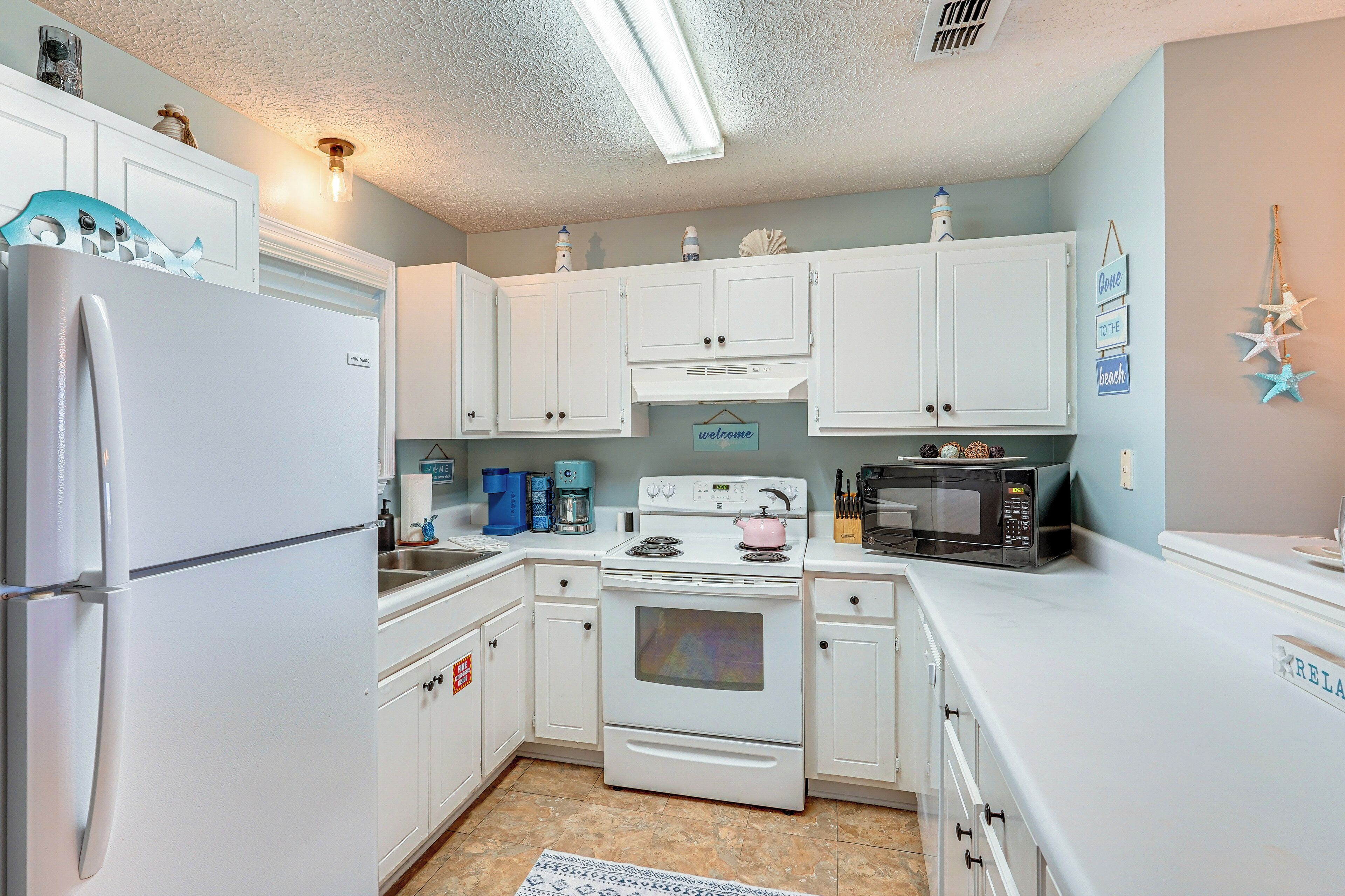 A kitchen with white cabinets, a refrigerator, a stove, a microwave, and a sink.
