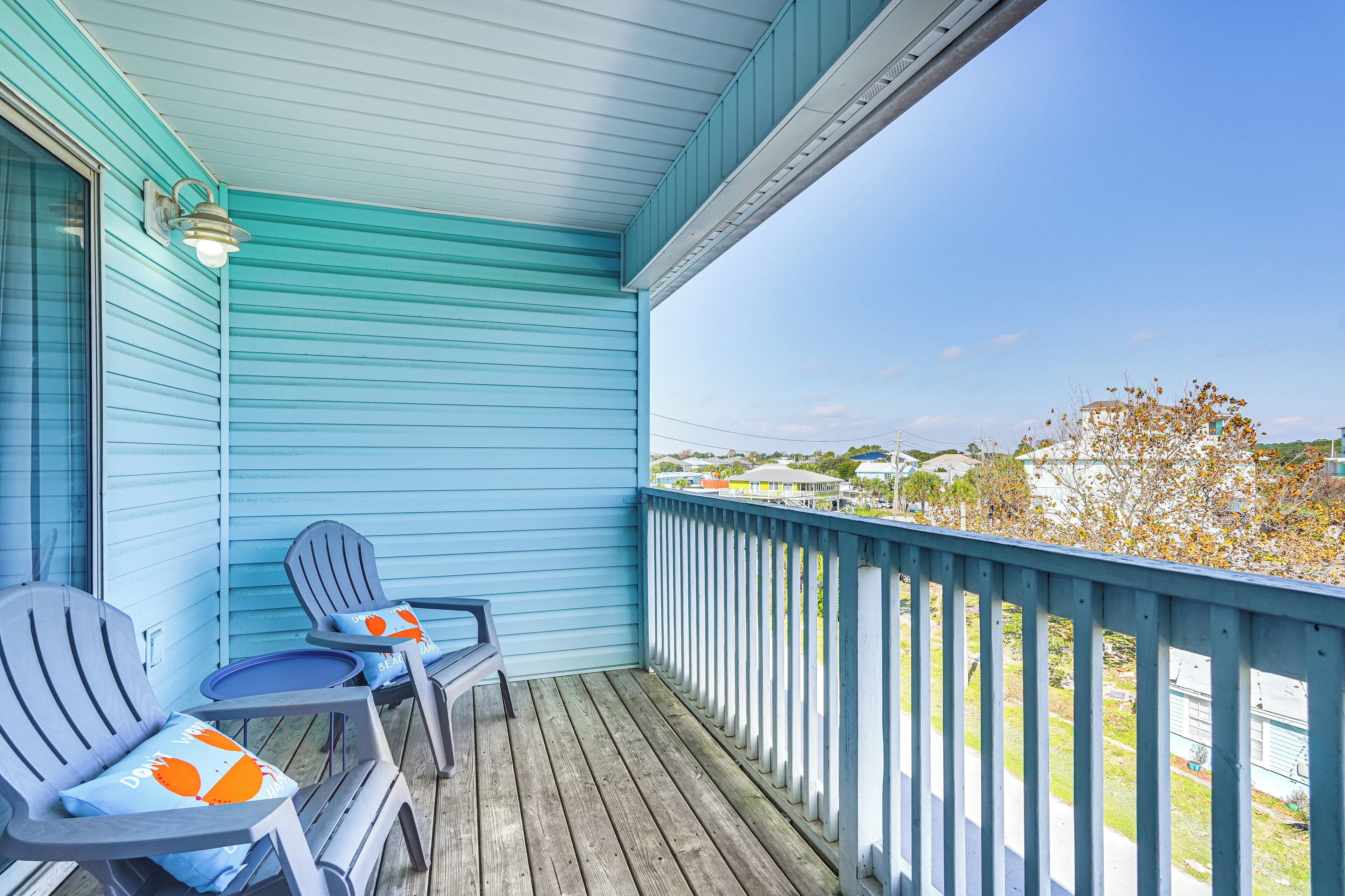 A blue porch with two Adirondack chairs and a small table, overlooking a residential area.