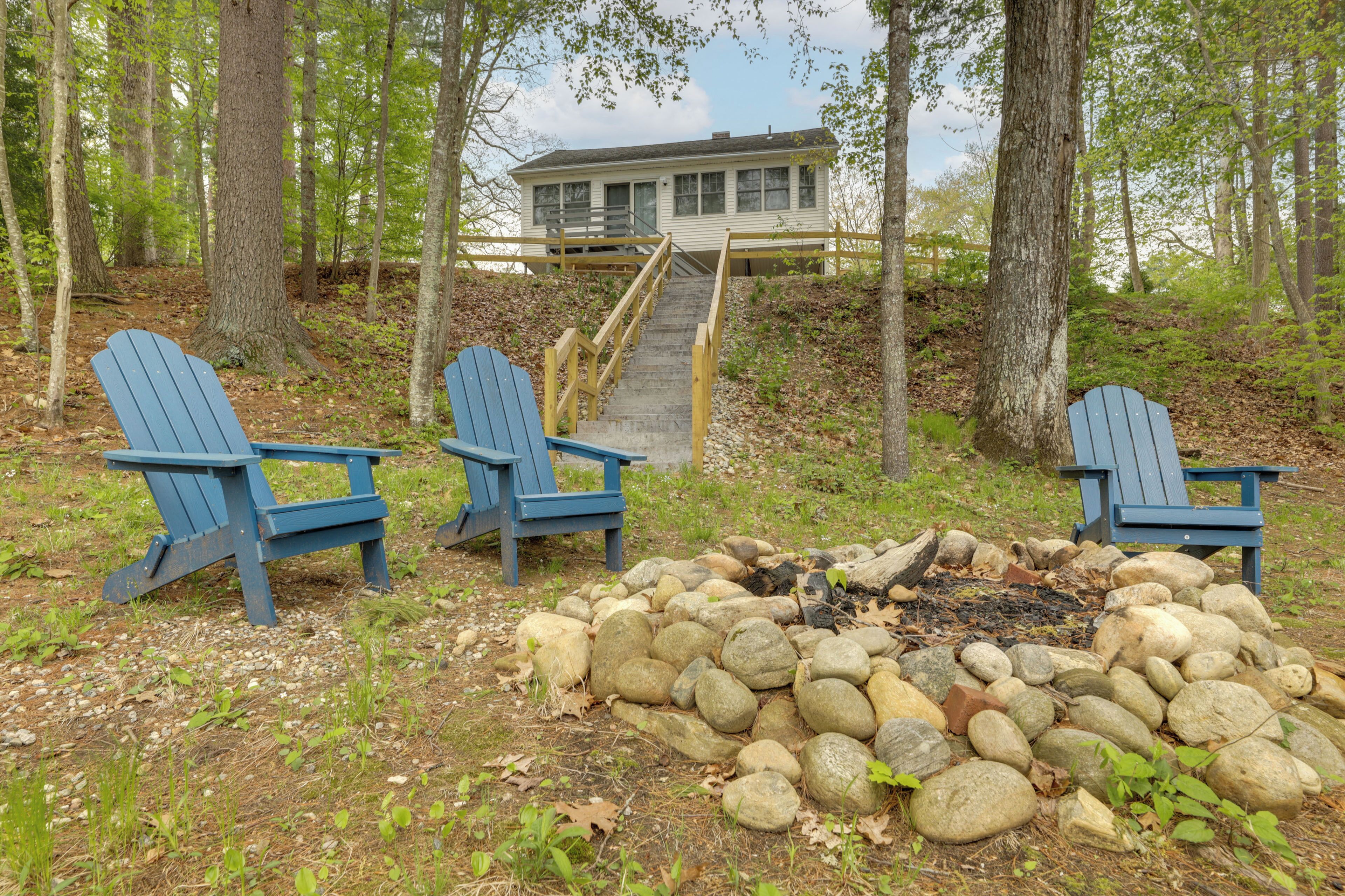 A cabin with a wooden deck, a fire pit with rocks, and two Adirondack chairs.