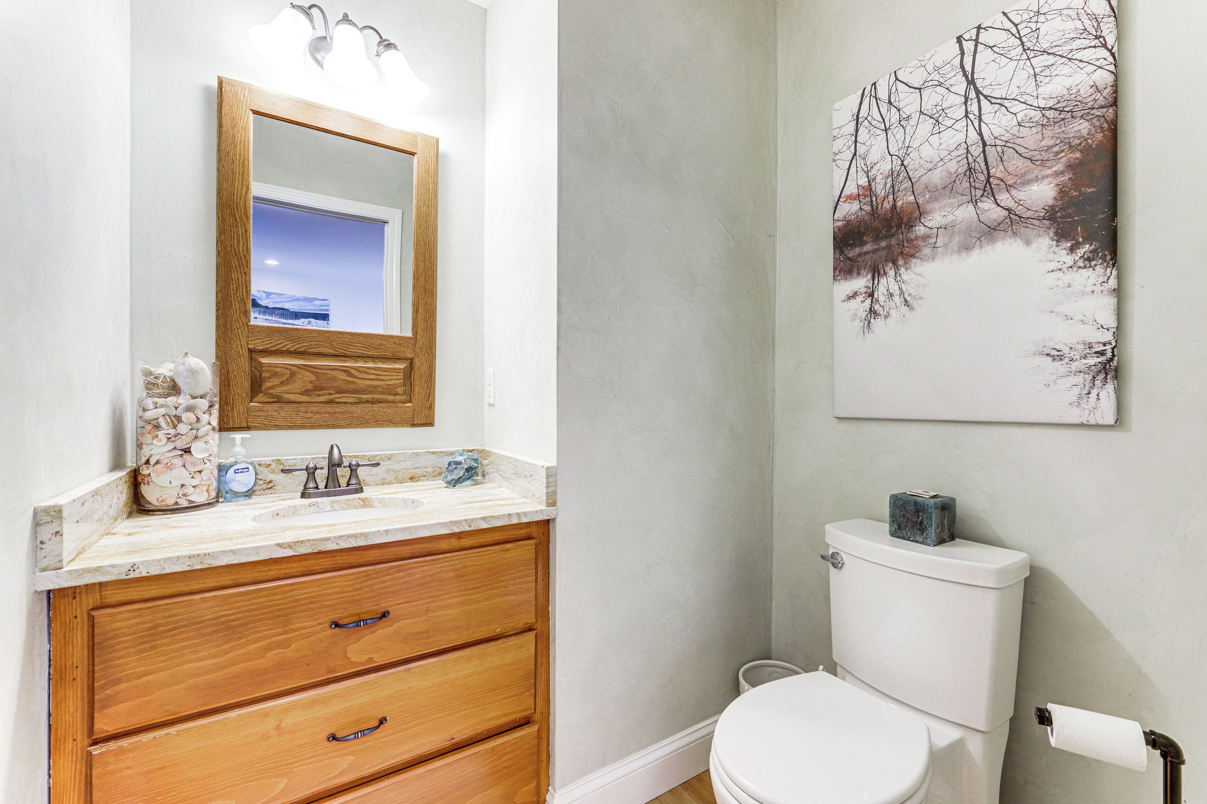 A bathroom with a wooden vanity, a white toilet, and a wall-mounted mirror.