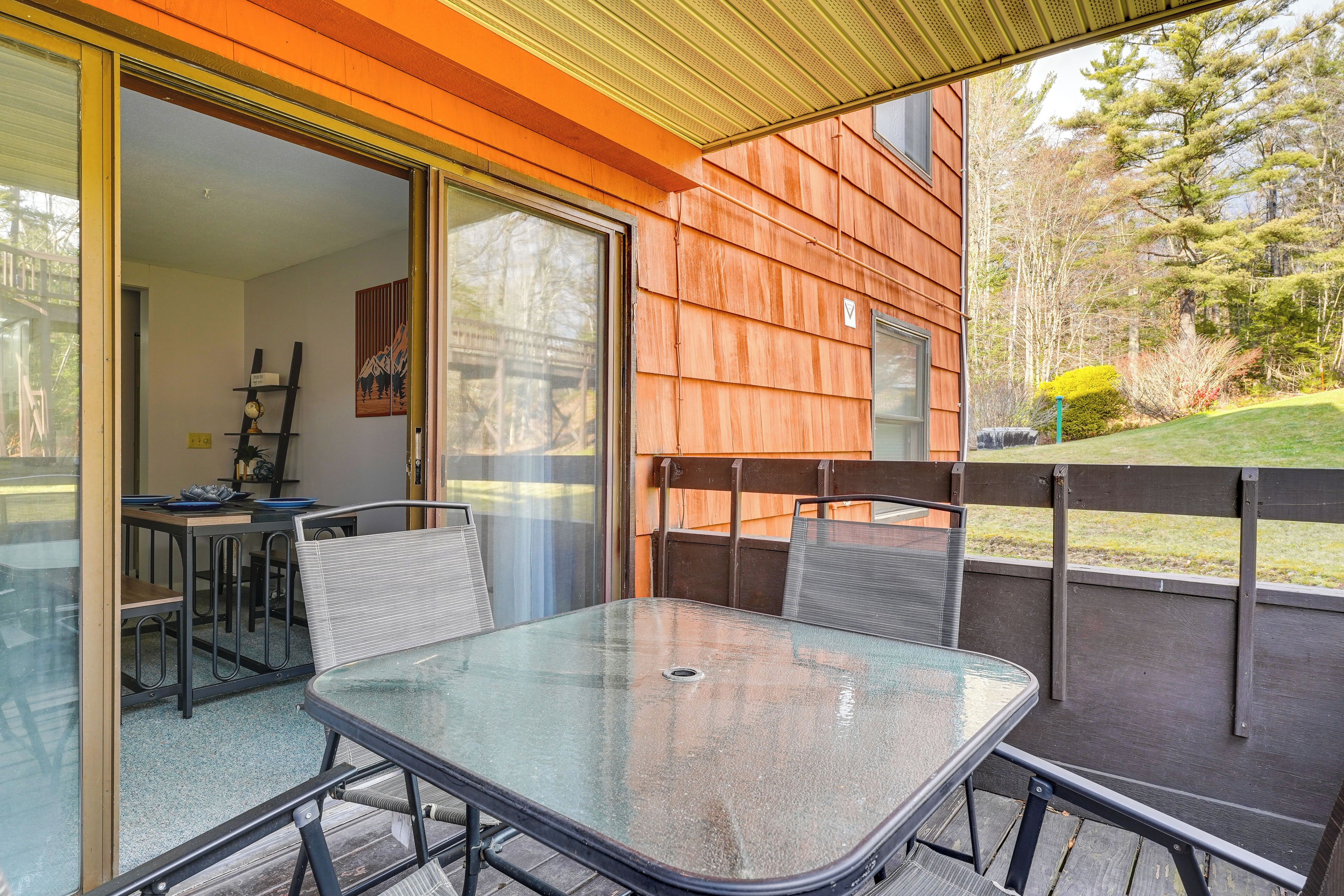 A glass-top table with metal chairs on a balcony with a wooden fence and a view of a garden.