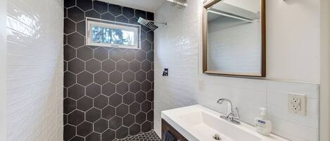 Une salle de bain moderne avec une douche carrelée de motifs hexagonaux, un lavabo blanc avec un miroir et une fenêtre située au-dessus de la douche.