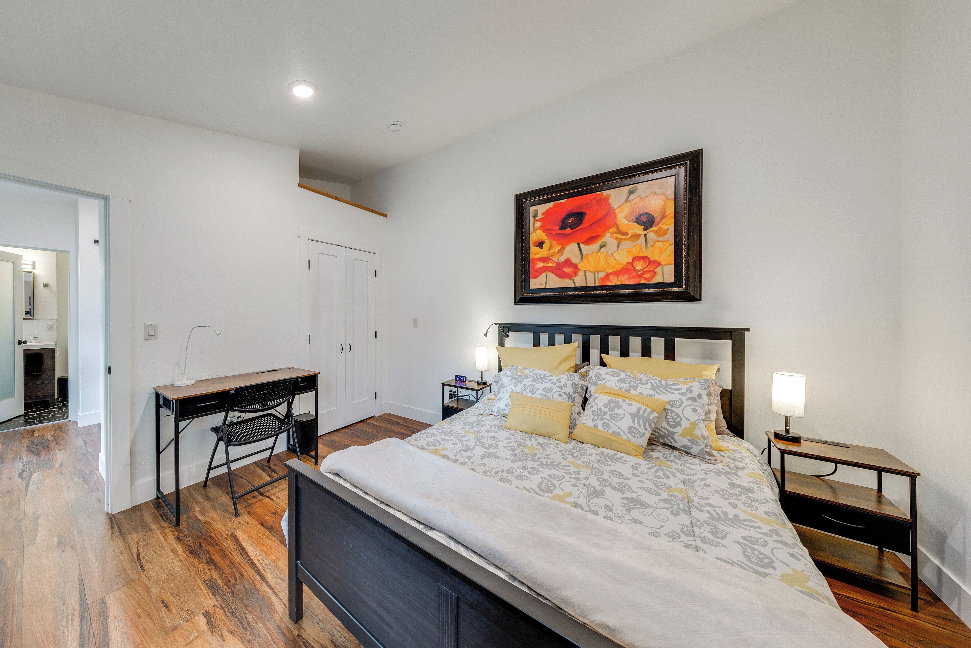 Une chambre à coucher avec un lit, un bureau, une chaise, une table de chevet et un tableau au mur.