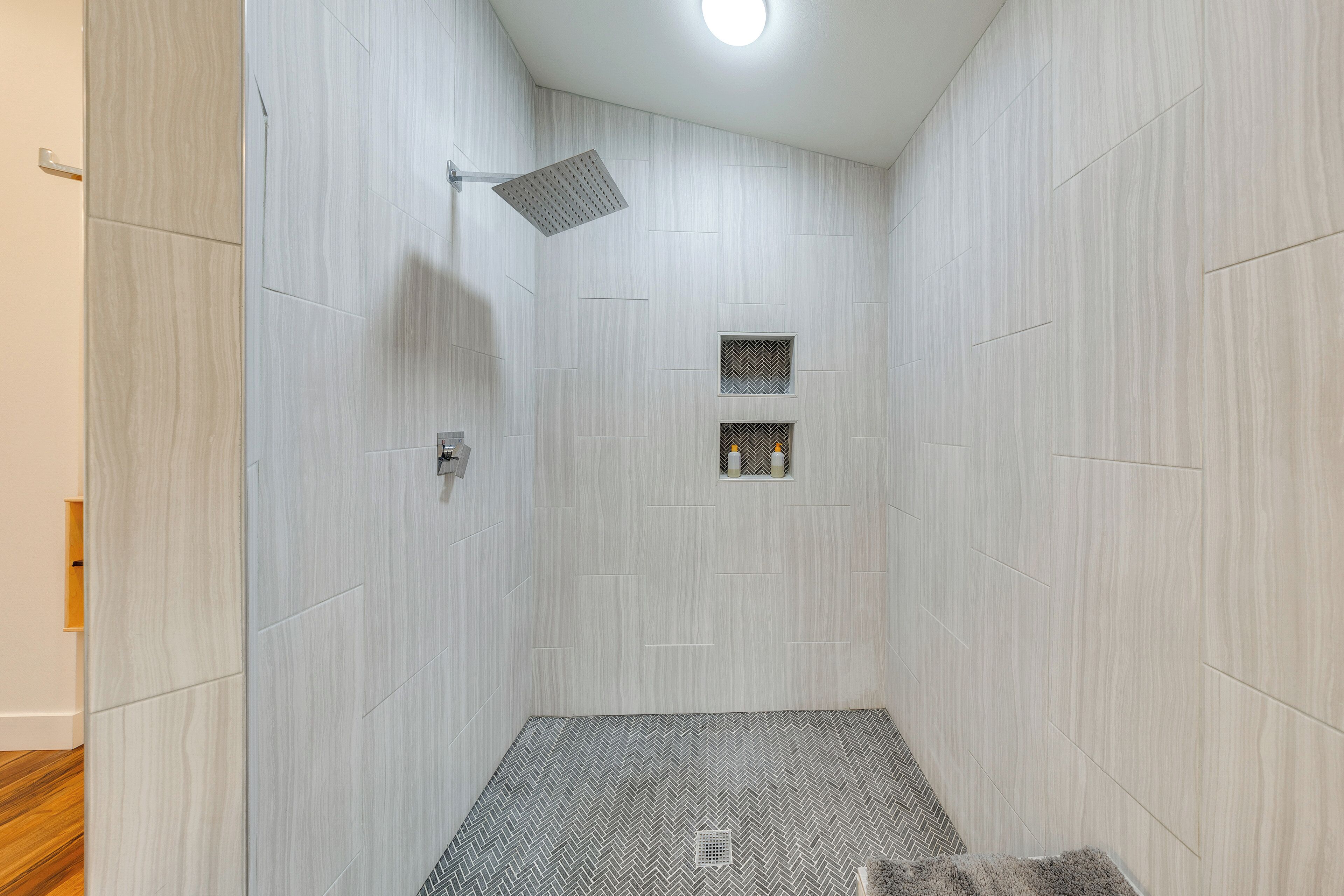 Un baño moderno con techo inclinado, un cabezal de ducha y una ventana pequeña.