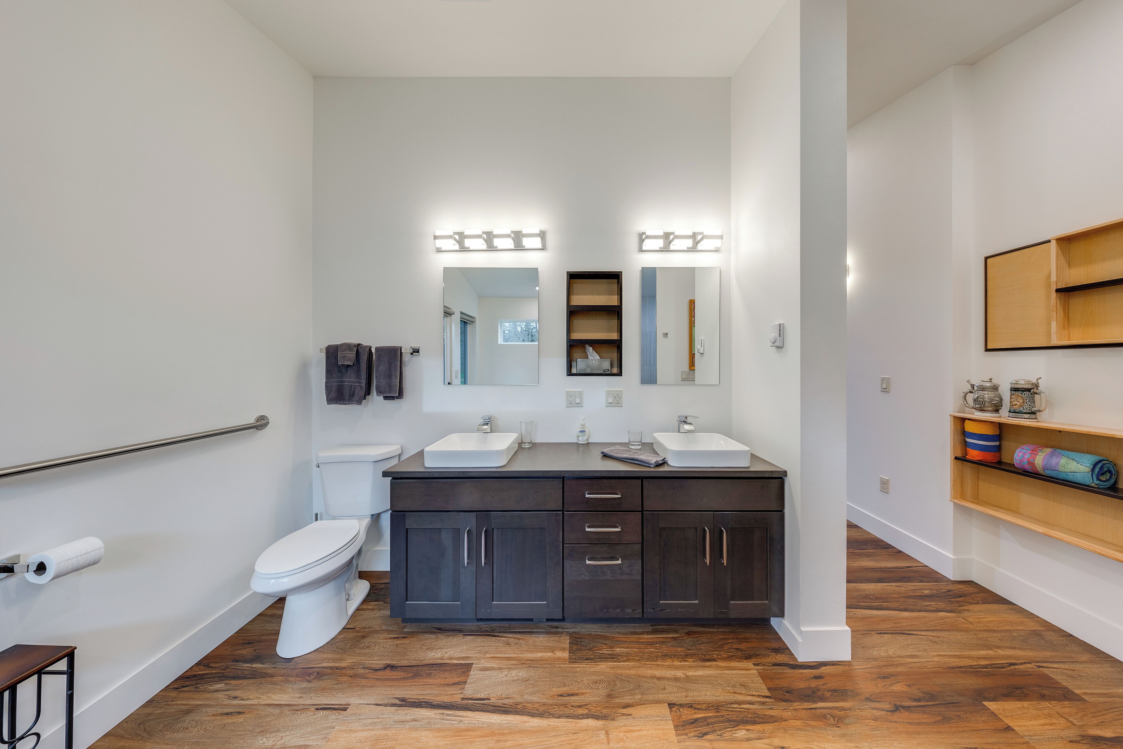 A modern bathroom with a dark wood vanity, two sinks, a toilet, and a shower area.