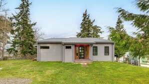 Una casa moderna de un solo piso con fachada gris, puerta principal roja y un pequeño porche.