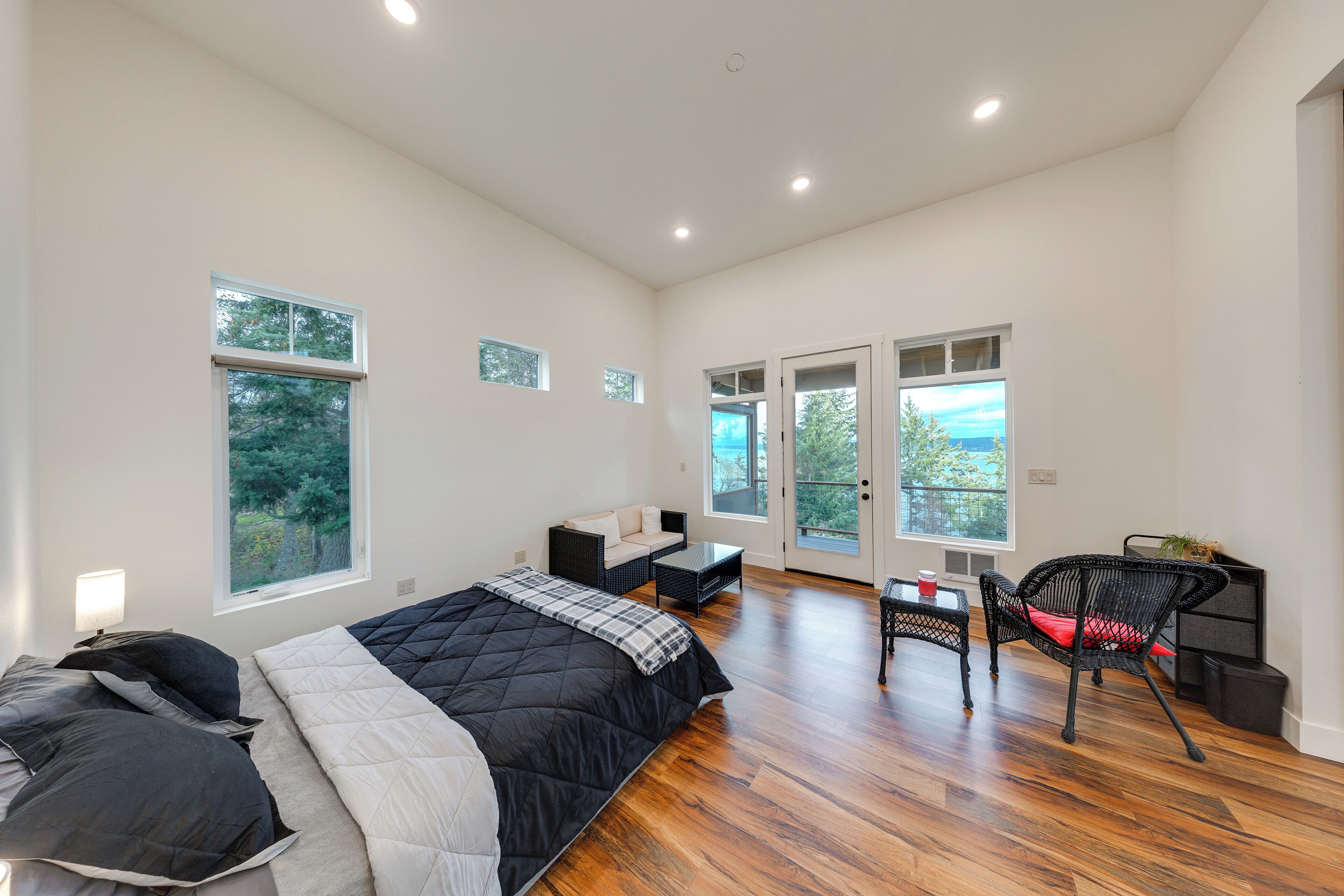 A spacious bedroom with a large bed, a seating area with a sofa and chairs, and multiple windows providing natural light and views of the outdoors.