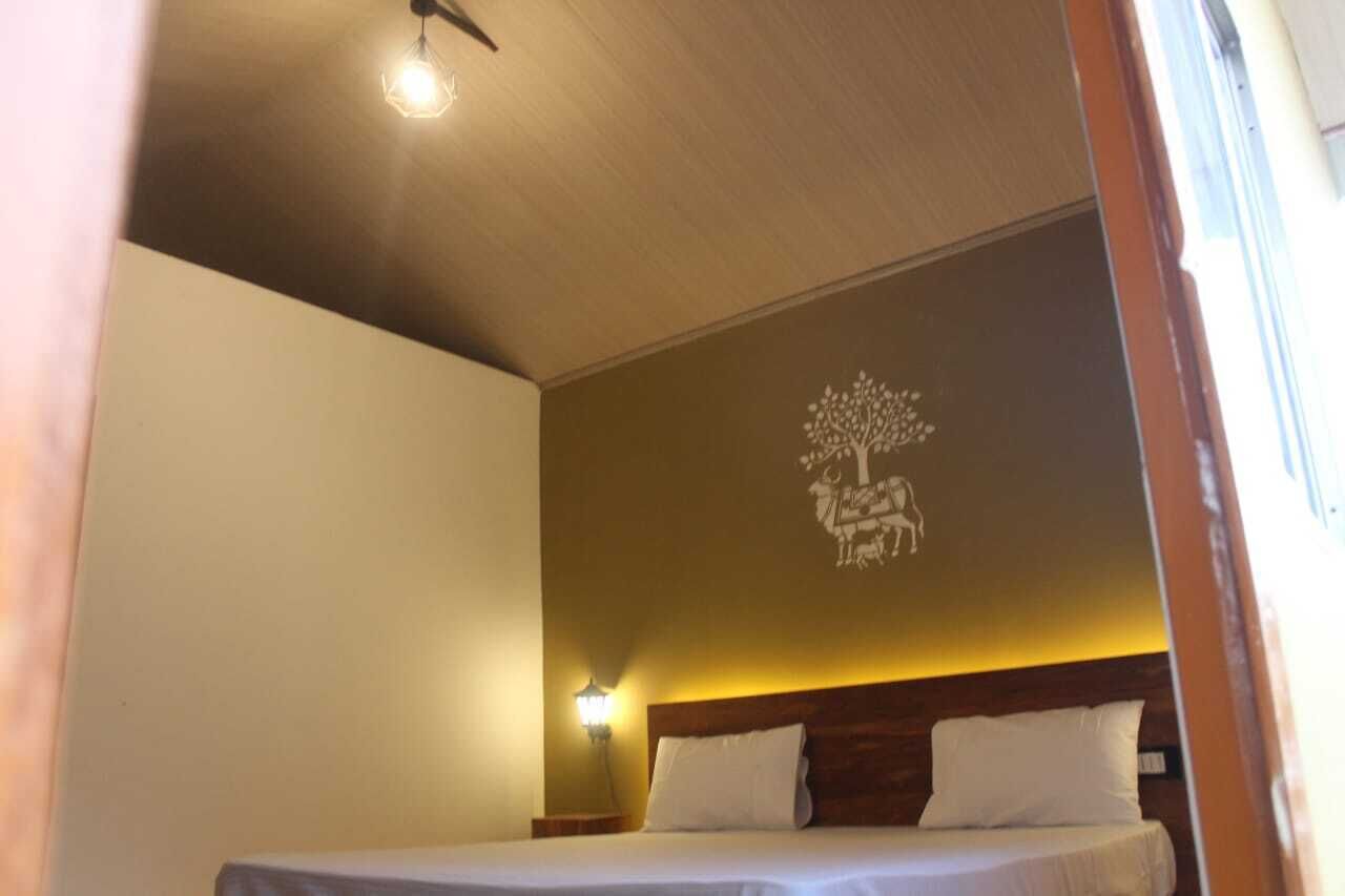 A bedroom with a bed, a wall-mounted light, and a decorative tree mural.