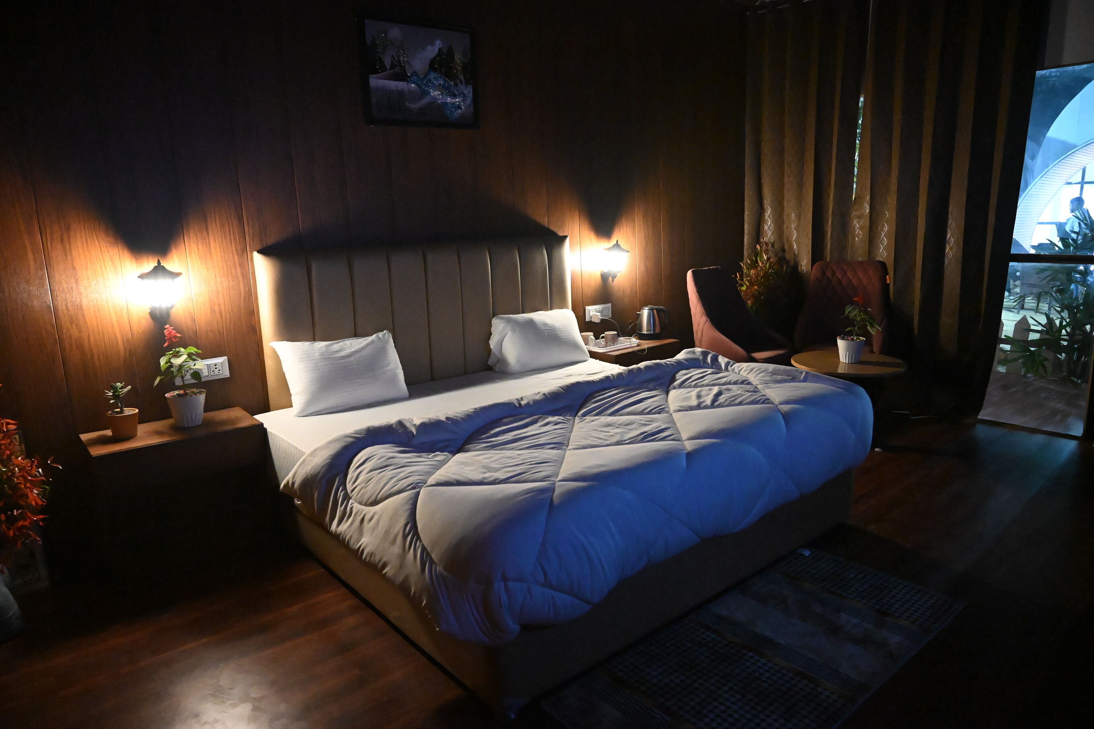 A modern bedroom with a large bed, two bedside tables with lamps, a chair, and a view of the outdoors.