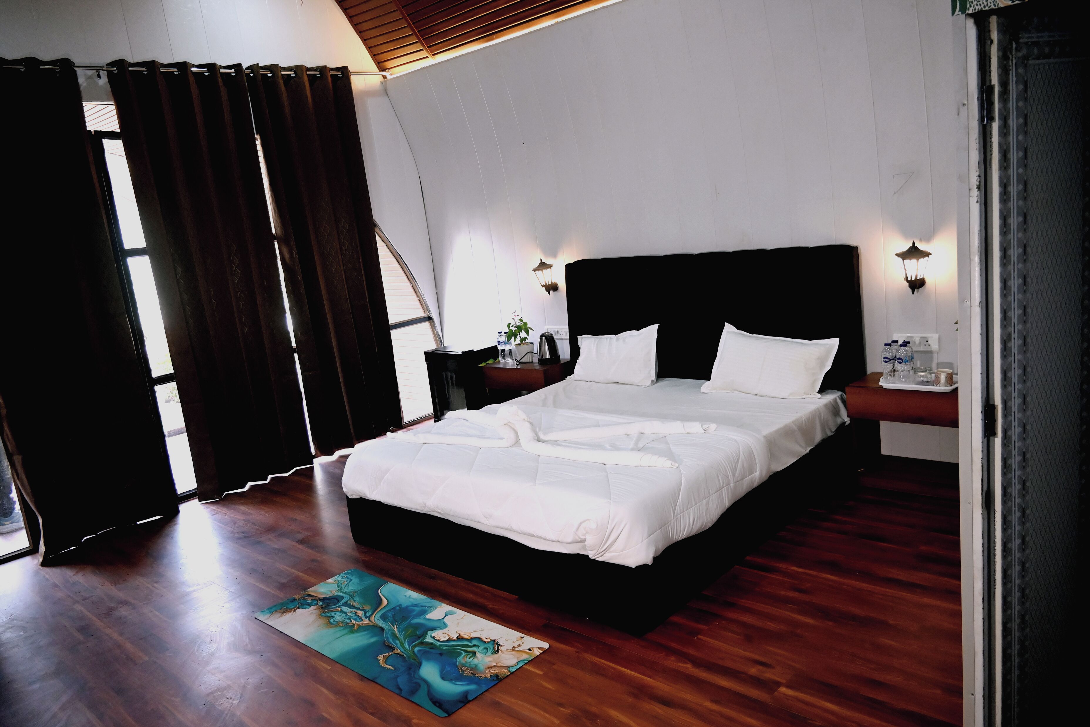 A bedroom with a large bed, wooden flooring, and a painting on the floor.