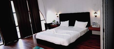 A bedroom with a large bed, wooden flooring, and a painting on the floor.