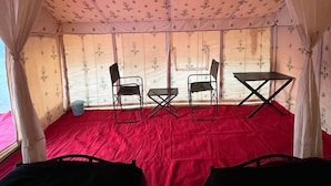A tent with a red floor, two chairs, a small table, and sheer curtains with a floral pattern. - Triveni Sangam Hotels And Resorts (Karchana)