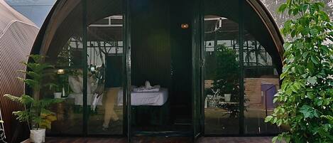 A modern, semi-open structure with a curved roof, a glass door entrance, and a wooden deck.