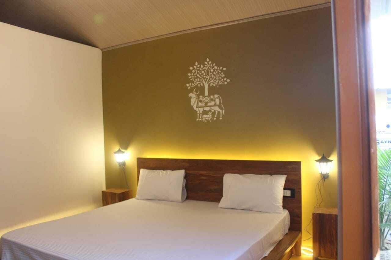 A hotel room with a bed, two bedside lamps, and a wall decoration of a tree with a figure.
