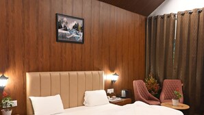 A modern bedroom with a large bed, wooden panel walls, a ceiling light, a nightstand, a chair, and a small table with a plant. - Triveni Sangam Hotels And Resorts (Karchana)