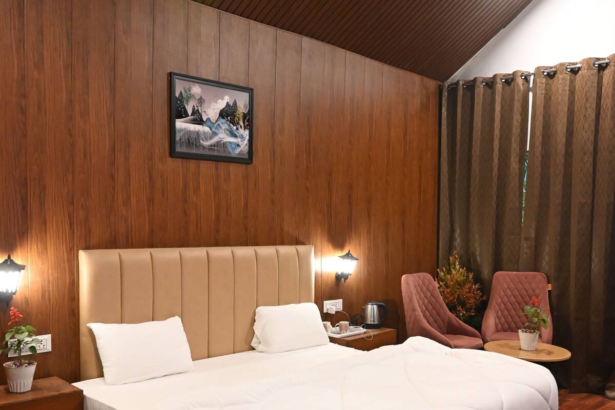 Een moderne slaapkamer met een groot bed, houten paneelwanden, een plafondlamp, een nachtkastje, een stoel en een bijzettafeltje met een plant.