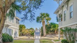 A pathway leading to a building with a covered walkway and palm trees. - Oceanfront Home w/ Private Beach Access + Soaring Views by Tybee Cottages (Tybee Island)