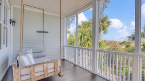 A porch with a swing chair, a wooden bench, and a view of palm trees and beach. - Oceanfront Home w/ Private Beach Access + Soaring Views by Tybee Cottages (Tybee Island)