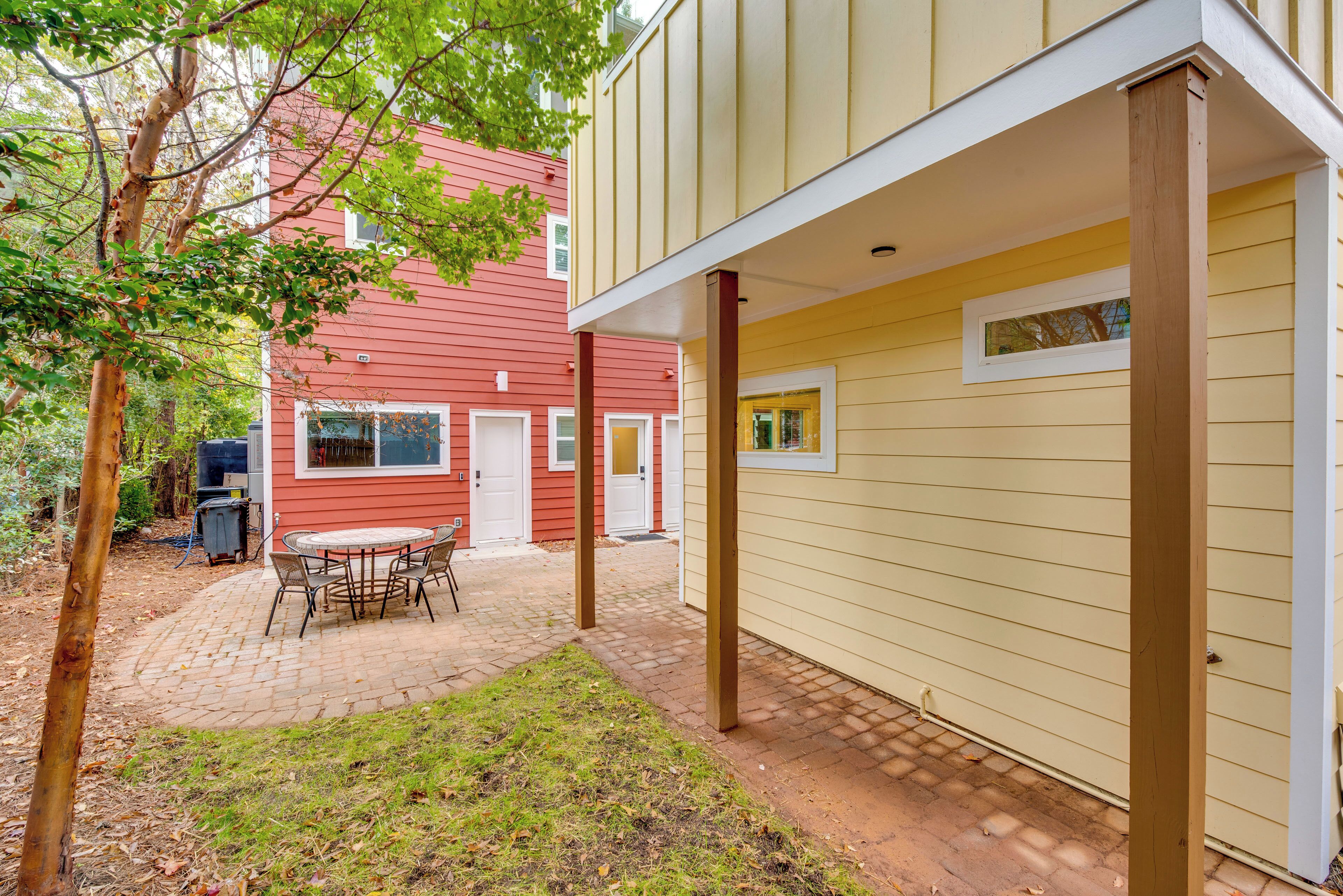 A patio with a table and chairs, a red house in the background, and a yellow building with windows.