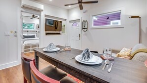 A dining area with a wooden table set for two, a ceiling fan, and a window with a view of trees.