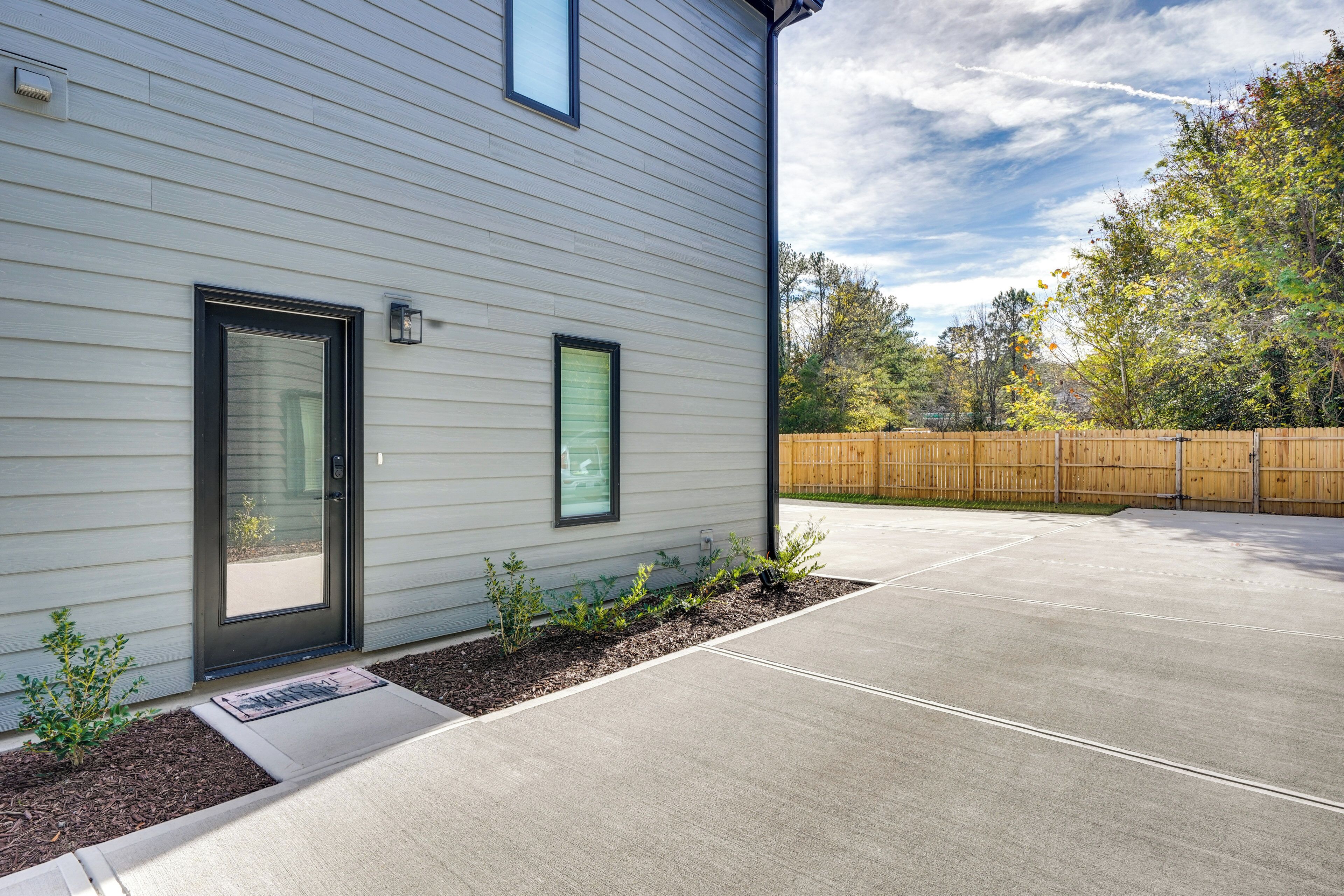 A modern house with a concrete driveway, a wooden fence, and a well-maintained garden.