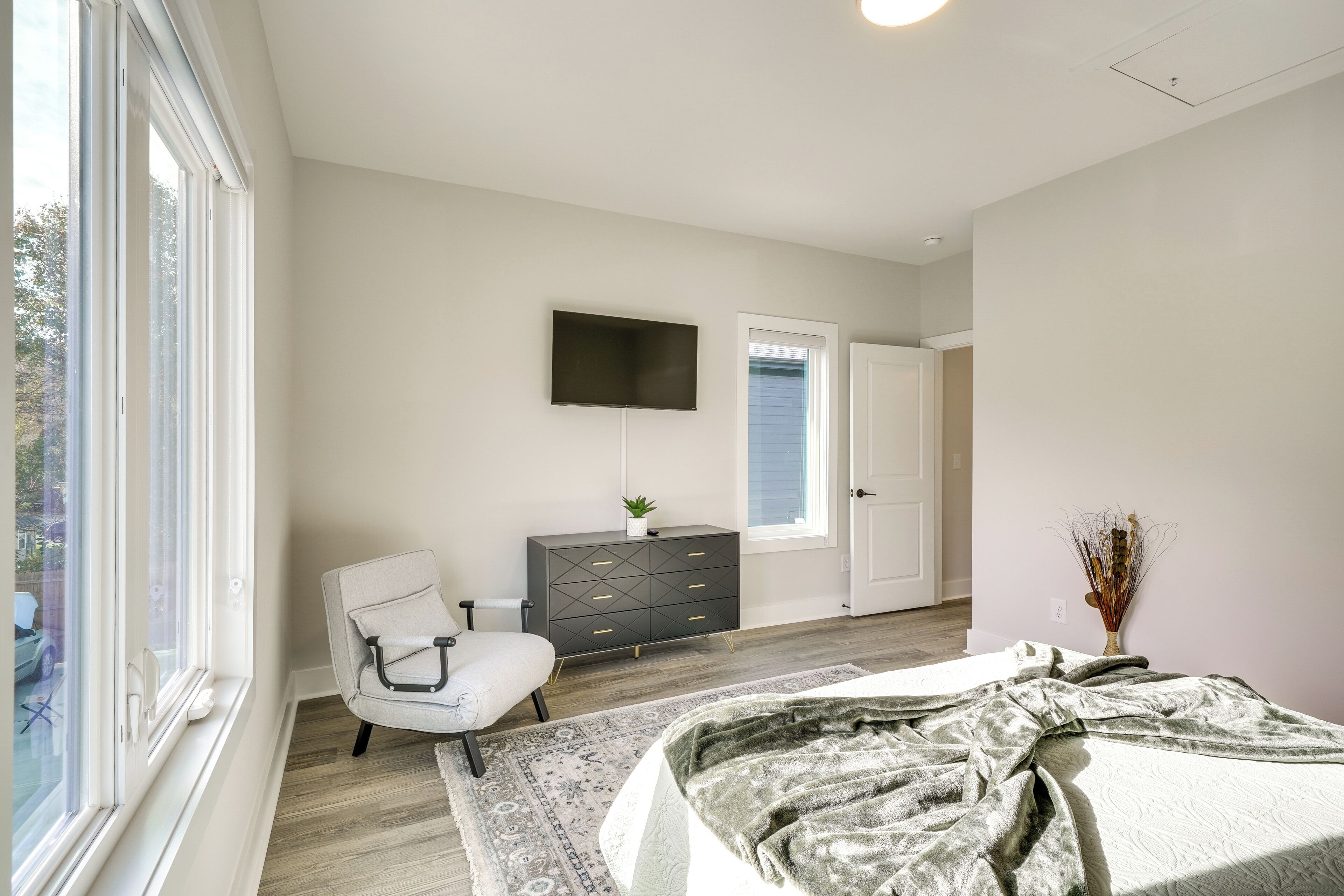 A bedroom with a bed, a chair, a dresser, a TV, and a window.