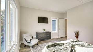 A bedroom with a bed, a chair, a dresser, a TV, and a window.