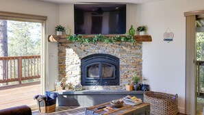 A stone fireplace with a TV above it, surrounded by plants and a wooden deck. - Ski, Hike & Fish: Mtn-view Gem w/ Deck in Tuolumne (Tuolumne)