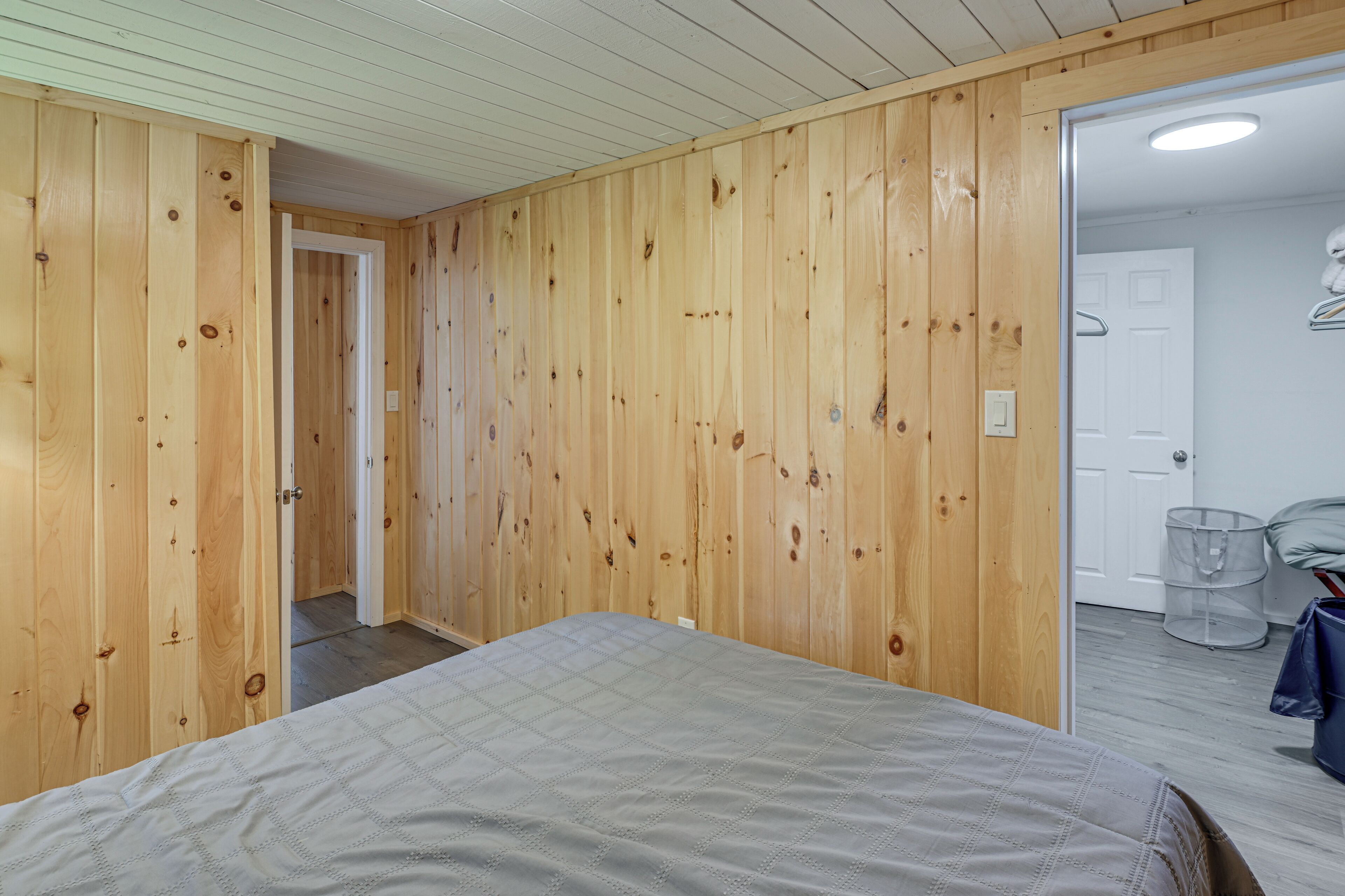 A bedroom with wooden walls, a bed, a door, and a white ceiling.