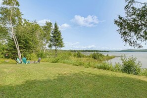 A lakeside view with a grassy area, trees, and a clear sky. - Waterfront Long Lake Retreat: Great for Families! (Sinclair)
