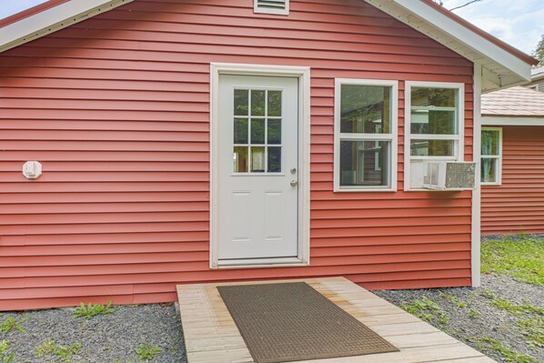 A red building with a white door, two windows, and an air conditioning unit.