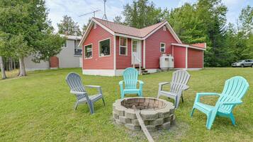 A red house with a fire pit and four Adirondack chairs in the yard.