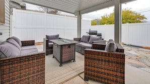 Een terras buiten met wicker meubels, een tafel met glazen blad en een barbecue.