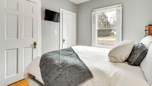 Quarto com cama, televisão fixada na parede e janela com persianas.