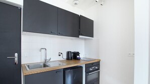 A compact kitchen with black cabinets, a wooden countertop, a sink, a coffee maker, and a refrigerator. - Apartment Boulogne Facing "les Passages" (Boulogne-Billancourt)