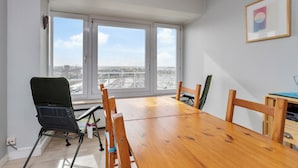 A room with a wooden dining table, chairs, a view through large windows, and a framed picture on the wall.