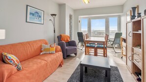 A modern living room with a sofa, chairs, a dining table, and a view of the city through large windows.