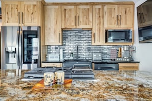 A modern kitchen with wooden cabinets, a stainless steel refrigerator, a microwave, and a granite countertop. - Scenic Waterfront Big Lake Home: Fish, Boat, Sled! (Big Lake)