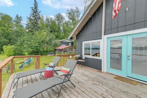 A deck with lounge chairs and a table, a turquoise door, and a red and white striped flag. - Scenic Waterfront Big Lake Home: Fish, Boat, Sled! (Big Lake)