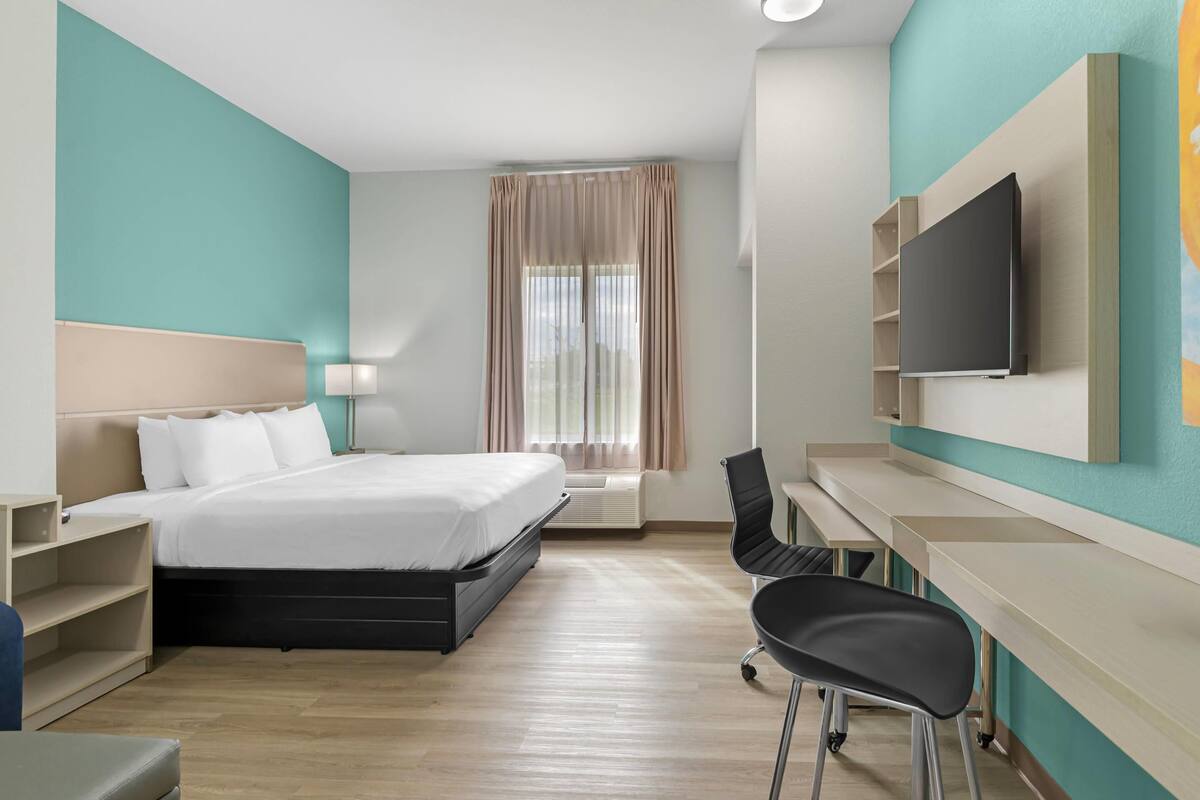 A hotel room with a bed, desk, chair, TV, and a window with curtains.