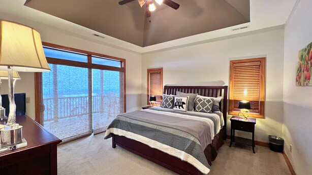 A bedroom with a large bed, a ceiling fan, a nightstand, a lamp, and a window with blinds. - exquisitely decorated two-bd loft condo, located in The Reserve- Mtn Views! (Sugar Mountain)