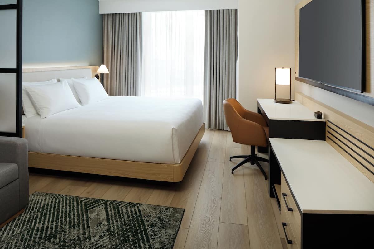 Habitación de hotel con cama, escritorio, silla, televisor y ventana con cortinas.