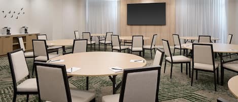 Una sala de conferencias con mesas y sillas redondas, una pantalla grande y una estación de café.