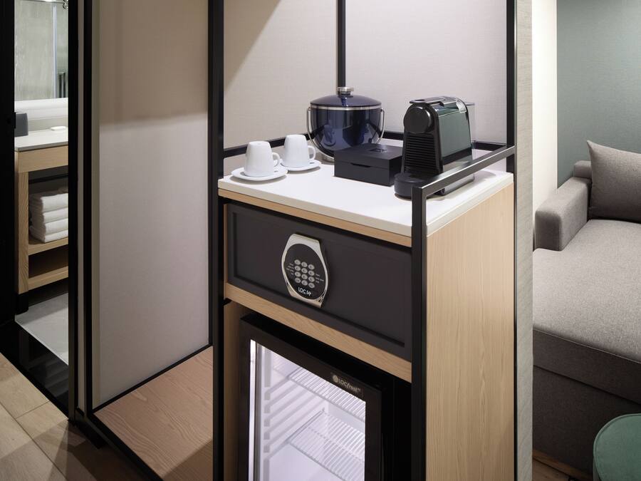 A compact hotel room with a kitchenette, a bed, and a green chair.