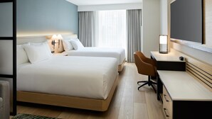 Habitación de hotel con dos camas, un escritorio, una silla, un televisor y una ventana con cortinas.