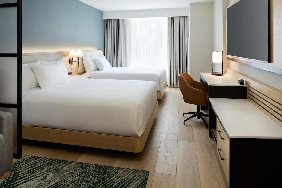 Habitación de hotel con dos camas, un escritorio, una silla, un televisor y una ventana con cortinas.