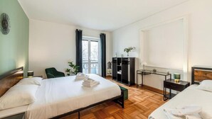 Ein Hotelzimmer mit zwei Betten, einem Schreibtisch, einem Stuhl, einem Kleiderschrank und einem Fenster mit Vorhängen.