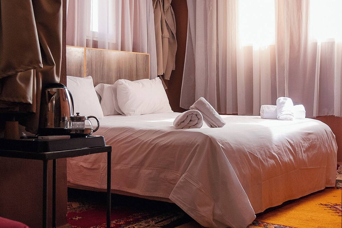 A hotel room with a bed, a bedside table with a coffee maker, and a window with curtains.