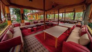 An outdoor seating area with red and beige sofas, wooden tables, and a patterned floor. - Couleurs Berbères (Lalla Takarkoust)