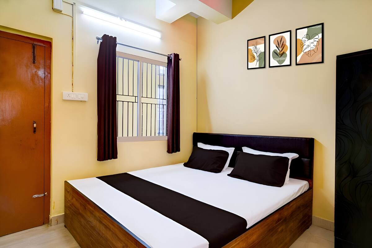 A neatly arranged bedroom with a wooden bed, a window with curtains, and three framed artworks on the wall.